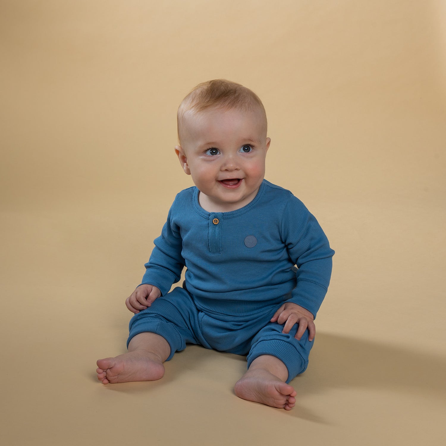 baby dreng iført sæt i økologisk bomuld med blå bukser og blå body med stolpelukning og træknap
